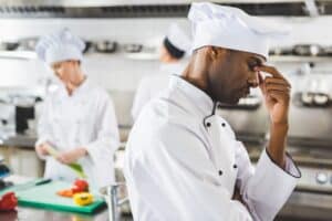 Tired African American Chef Touching Nose Bridge At Restaurant Kitchen